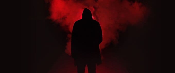 A silhouette of a hooded figure appears to watch a cloud of red smoke
